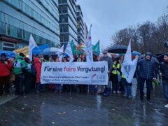 Protestmenschenmenge mit Banner. Schriftzug Für eine faire Vergütung. Logo des Berufsverband der freien Berufsbetreuer*innen BdB