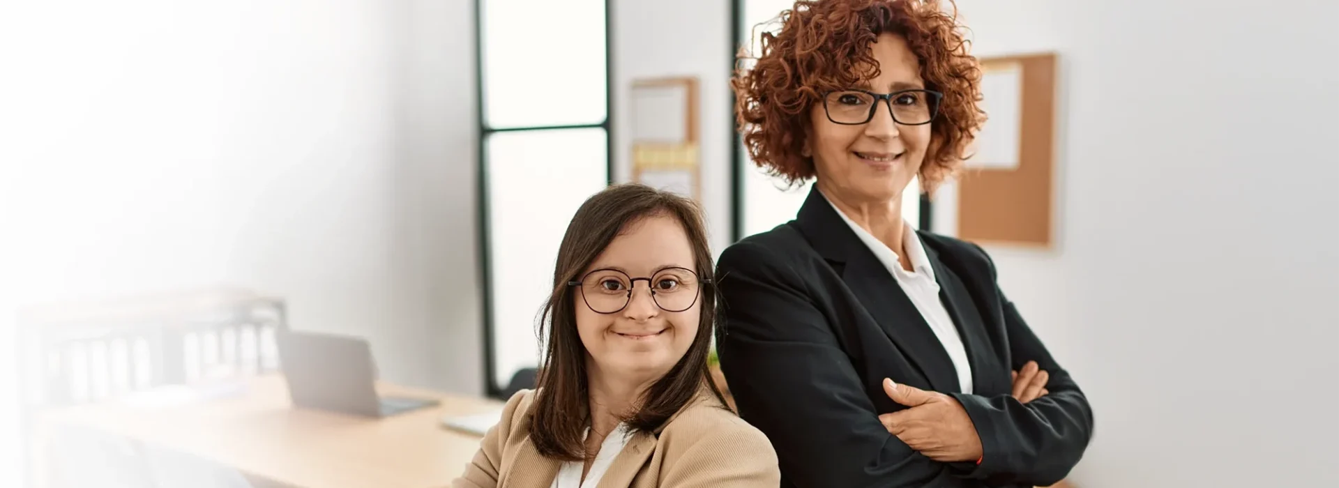 2 Frauen arbeiten im Büro. Fachfrau und Frau mit Down-Syndrom arbeiten als inklusives Team.